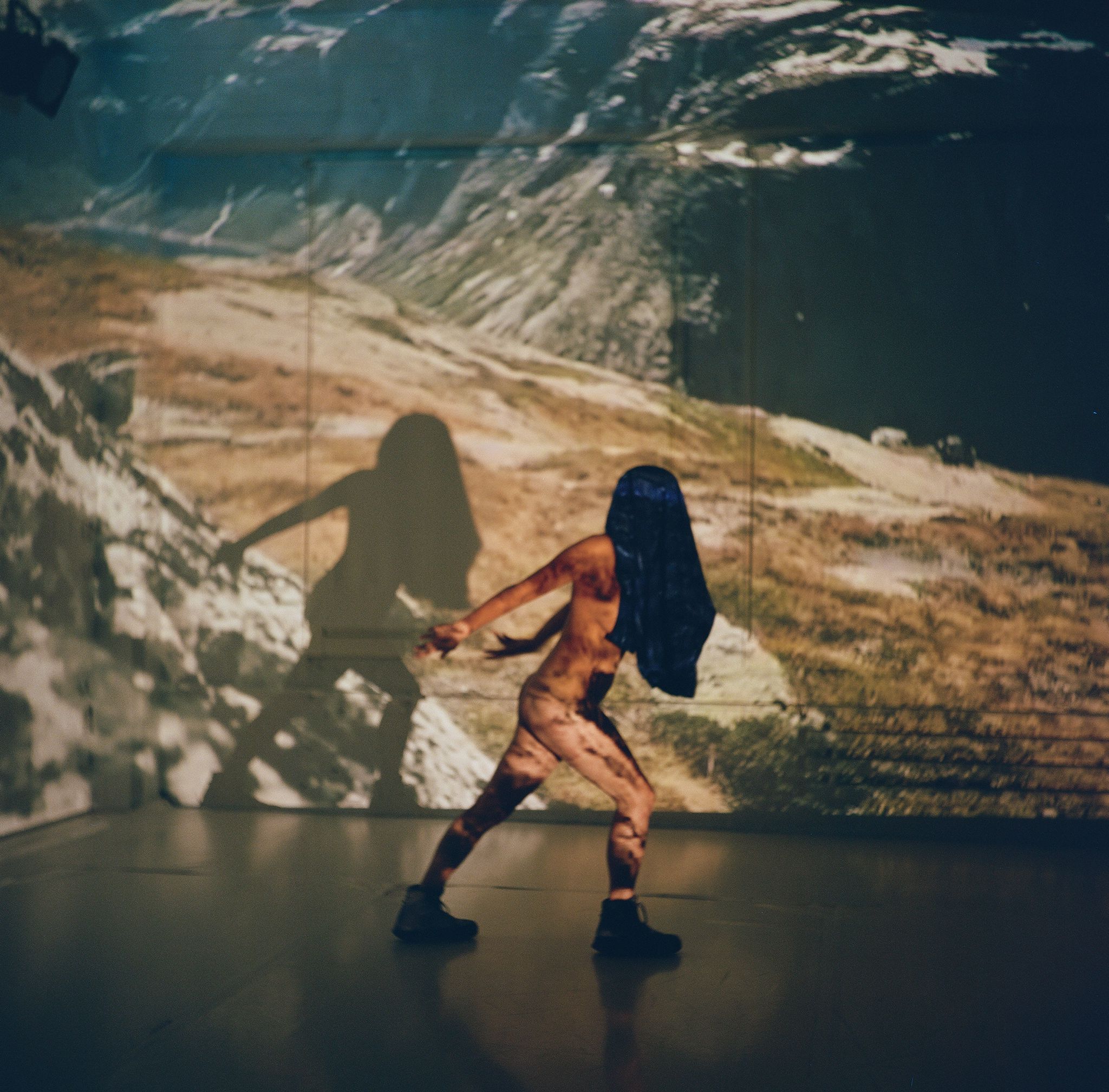 A naked woman in hiking boots with a blue jacket over her head