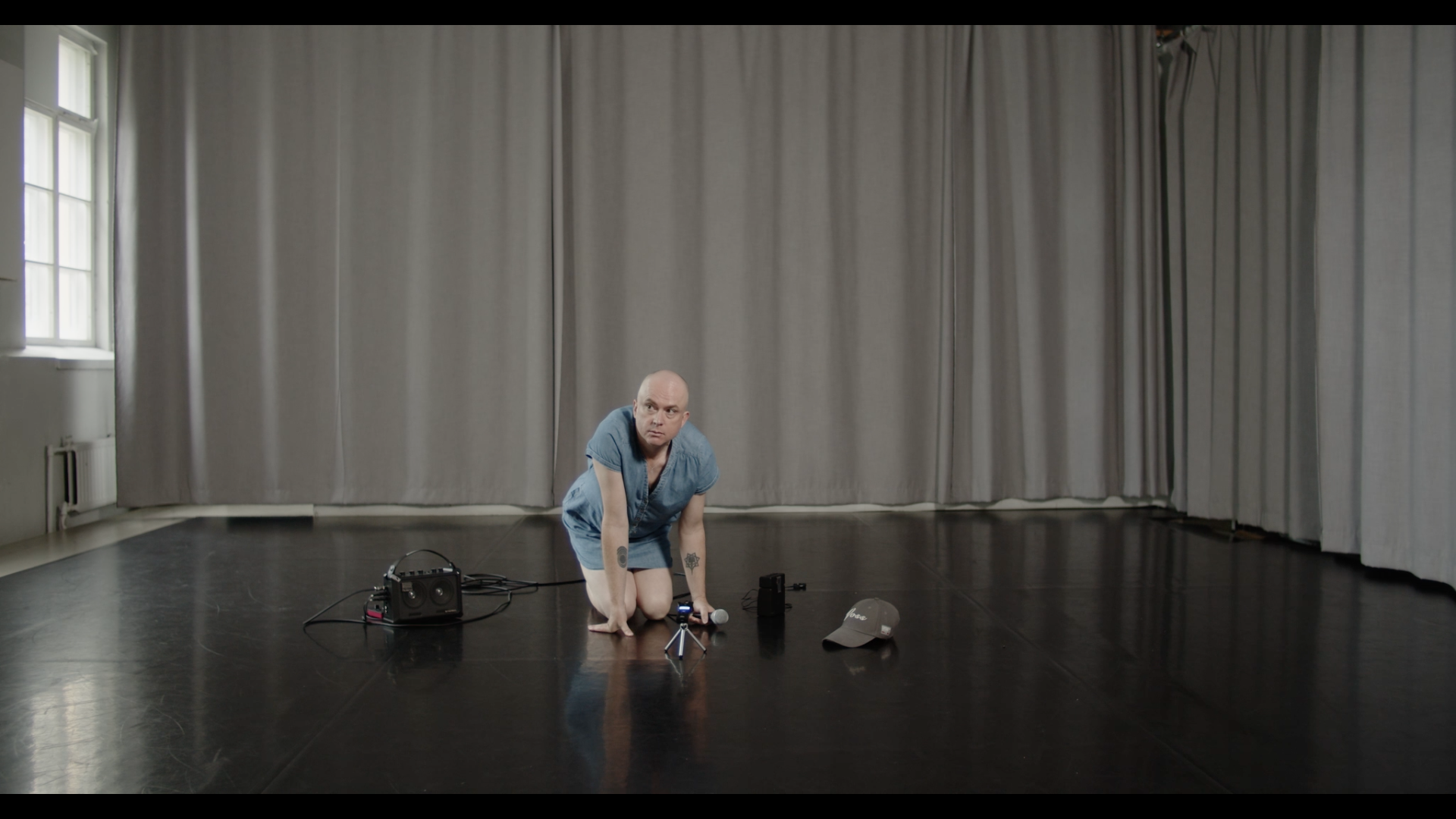 A trans woman in a denim dress crouches on the floor with a microphone in her hand